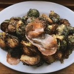 a white plate topped with brussel sprouts and ham.
