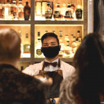 a man wearing a face mask standing in front of a bar.