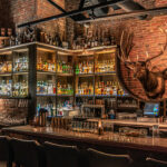 a bar with lots of liquor bottles and a deer head on the wall.