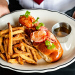 a person holding a plate with a lobster sandwich and french fries.