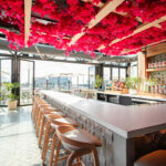 a bar with a lot of stools and flowers hanging from the ceiling.