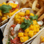 a close up of three tacos on a plate with french fries.