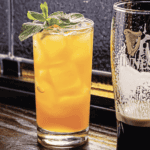 a tall glass with a mint garnish sits next to a tall glass with.